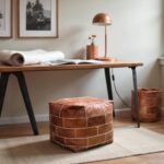 Square leather floor pouf as footrest under wooden desk, showcasing cognac leather with geometric cream stitching