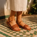 Leather sandals with hand-braided tan straps, worn on Moroccan mosaic tiles in warm sunlight.