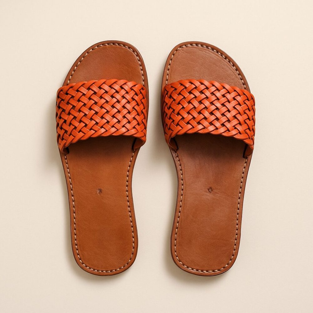 Studio shot of vibrant orange woven Leather Slides on neutral background.
