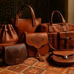 Collection of authentic handmade Moroccan leather bags in various styles including crossbody, tote, and embossed designs displayed on traditional Berber carpet
