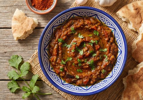 Traditional Moroccan zaalouk eggplant and tomato dip in a ceramic bowl garnished with fresh cilantro and olive oil, served with crusty bread