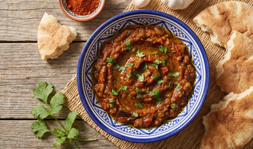Traditional Moroccan zaalouk eggplant and tomato dip in a ceramic bowl garnished with fresh cilantro and olive oil, served with crusty bread