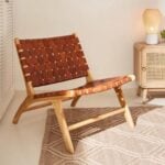 Leather lounge chair in tan with teak frame beside wooden cabinet in warm interior space