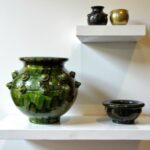 Green ceramic vase 30cm with decorative studs on floating shelf alongside smaller pottery pieces