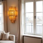 Natural tiered handwoven raffia wall sconce with warm amber glow in minimalist corner setting with curtains