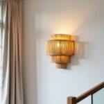Four-tier handwoven raffia wall sconce mounted on wall near staircase with warm ambient lighting