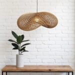 Handwoven rattan pendant lamp with organic wave design over wood table and white brick wall accent