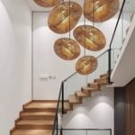 Multiple handwoven rattan pendant lamps cascading over modern staircase creating sculptural lighting display