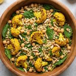 Mixed Moroccan cauliflower couscous bowl with turmeric-roasted cauliflower, chickpeas, pearl couscous, fresh herbs, and toasted almonds in a wooden serving bowl
