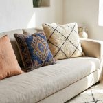 An assortment of handmade Moroccan pillow covers, including cactus silk and wool Kilim styles with geometric patterns, layered on a sofa in a bright, modern room.