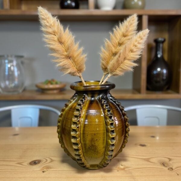 Handmade ceramic vase 30cm with raised patterns in amber brown glaze holding dried pampas grass on wooden table