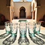 Aqua handblown diamond tea glasses arranged on a table in a traditional Moroccan riad with arched architecture