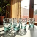 Recycled aqua handblown diamond tea glasses on a sunlit stone windowsill casting shadows through the glass