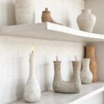 Handmade ceramic double candleholder with U-shaped design, displayed on white shelf among neutral pottery vases