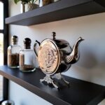 Ornate decorative silver teapot display on modern shelf with dark background and decorative glass bottles