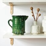 Rustic handmade ceramic pitcher with glossy green glaze and vertical ribbing, styled with dried botanical stems