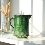 Moroccan Tamegroute ceramic pitcher in deep green glaze with textured botanical patterns on white shelf