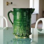 Close-up of handcrafted ceramic pitcher showing rich green glaze variations and weathered embossed detailing