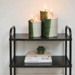 Multi-wick ceramic candle holders with signature green glaze arranged on black metal shelf with books