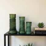 Green glazed ceramic candleholders set of 3 with stacked pillar design on black shelf with plant and books