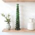 Green glazed ceramic candle holder with spiral tower design on wooden shelf with plants