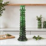 Dark green glazed ceramic candle holder tower on white countertop with small plant accent