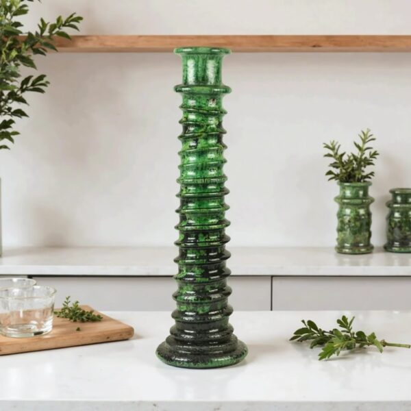 Dark green glazed ceramic candle holder tower on white countertop with small plant accent