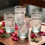Close-up of white geometric tea glasses featuring hand-painted Moroccan lattice and rose petals on recycled glass