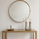 Ceramic double candleholder in warm beige tone beneath round mirror, styled on gold console table