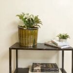 Large rustic ceramic planter with vertical ribbing and white flower arrangement on metal console table with books