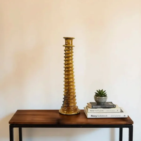 Golden brown ceramic candle holder with architectural grooves on modern wood and metal table