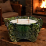 Lit triple-wick candle in green ceramic vessel by fireplace