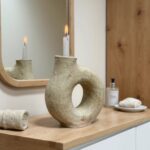 White ceramic candle holder with distinctive ring form on wooden vanity, handcrafted pottery reflected in mirror