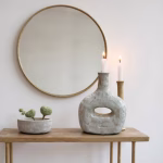 Minimalist gray bottle candleholder on wooden table with round mirror