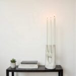 Modern sculptural ceramic candle holder with three lit candles displayed on black shelf with books
