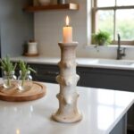 Handcrafted ceramic candlestick tower 40cm tall with textured white finish and burning taper candle on kitchen counter