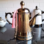 Moroccan brass coffee pot with silver plating against white wall