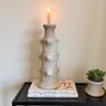 Tamegroute pottery ceramic candlestick tower in white with lit candle on stacked books next to succulent planter