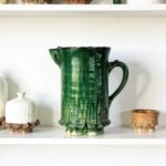 Antique-style green ceramic pitcher on white shelf alongside ivory and tan Moroccan pottery pieces