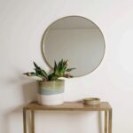 Artisan ceramic indoor planter with tulips beneath brass round mirror on console