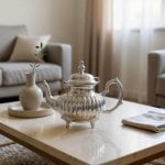 Silver ribbed teapot on marble coffee table beside white ceramic vase in modern living room setting
