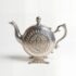 Disc shaped silver-plated decorative silver teapot display with octagonal geometric medallion and ornate splayed feet