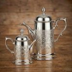 Handcrafted Moroccan silver coffee server set featuring large and small pots with intricate geometric engravings displayed on rustic wooden table