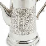 Close-up detail of traditional hand-engraved arabesque patterns on a Moroccan silver coffee server showing floral and geometric motifs