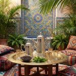 Silver coffee server set styled in traditional Moroccan riad with zellige tile backdrop, brass tray, mint tea glasses, and colorful Berber cushions