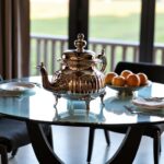 Handcrafted ribbed silver teapot ornate design with polished finish on glass table with fruit bowl background