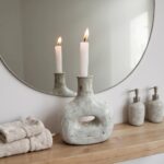 Close-up of ceramic candle holder bottle with lit candles, weathered gray finish and architectural cutout