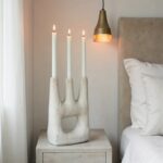 Triple ceramic candle holder with lit tapers on bedside table in Scandinavian-style bedroom