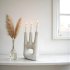 White ceramic candle holder with abstract hand design holding three taper candles on minimalist windowsill