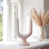 Handcrafted ceramic candle holder in white with twin arc design on windowsill with pampas grass decor
